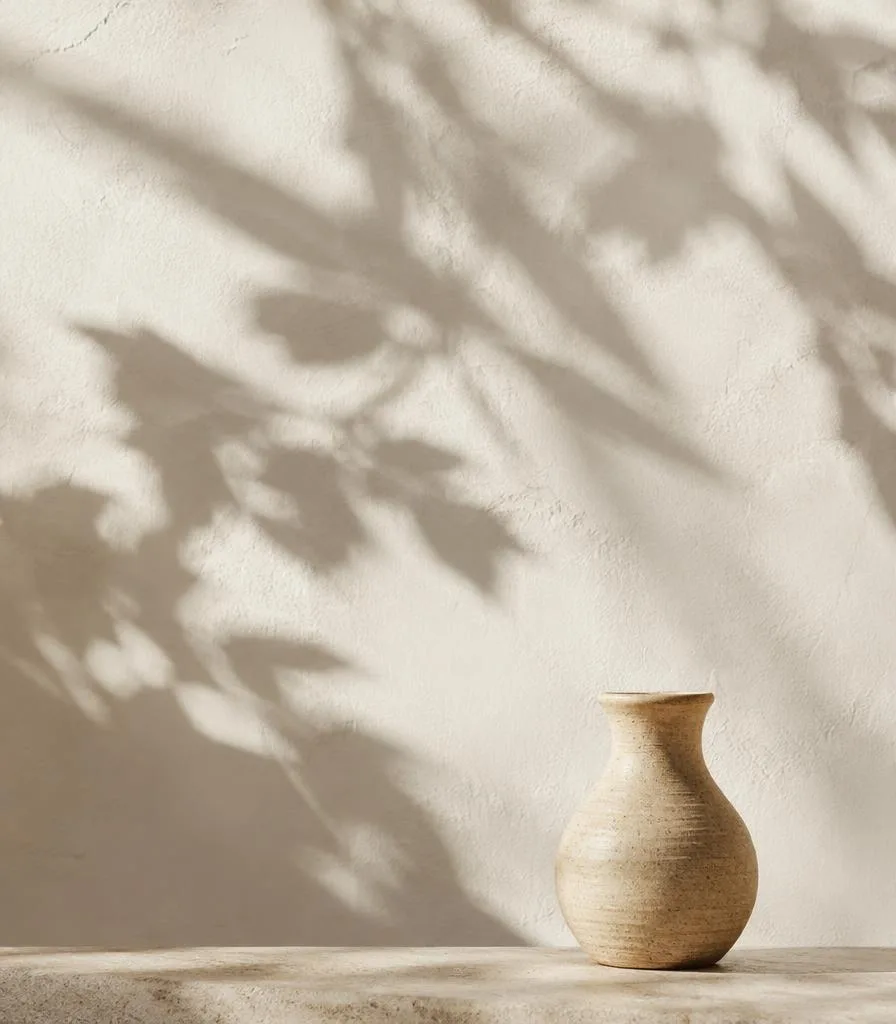 Leaf shadows on an ivory wall above a small ceramic vase